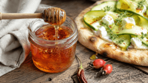 Zelfgemaakte rozenbottel-hot-honey met chilivlokken bij een flatbread met courgette en geitenkaas.