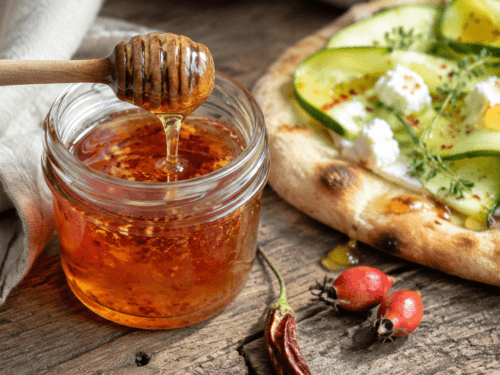 Zelfgemaakte rozenbottel-hot-honey met chilivlokken bij een flatbread met courgette en geitenkaas.