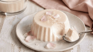 Romige hondsroosbloesem-panna cotta met roze hondsroosblaadjes en vers zomerfruit op een rustieke tafel